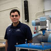 Omar Aboul-Enein poses next to a silver and blue robotic arm in a lab setting.
