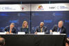 Four officials sit at a table signing documents in front of banners for the NIST National Cybersecurity Center of Excellence.