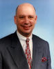 A headshot style portrait of a man in a gray suit.