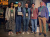 Five people dressed in business casual and wearing conference badges on lanyards pose with a framed award certificate.