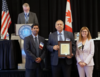 David Sefcik (center) accepting his award from NCWM Chair-elect Gene Robertson (at the podium), NCWM Chair Mahesh Albuquerque (left) and NIST Director Laurie Locascio (right).