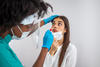 A medical worker wears gloves as she prepares to swab the nose of a female patient. 