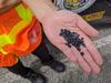 Someone wearing a safety vest holds up a handful of black plastic pellets.