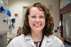 Wearing safety glasses and a lab coat, Jerilyn Izac poses for a portrait in the lab