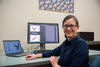 Melinda Kleczynski poses sitting at her desk, with a monitor showing data and graphs behind her. 