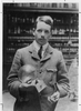 Historical photo shows Henry Moseley in a lab holding a glass globe on a stand. 