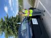 Jennifer Helgeson, holding a clipboard and wearing a high-vis vest stands next to a car. The car has a large sign on the side that reads “Center for Community Resilience Planning. Lumberton, NC Flood Study Team.” 