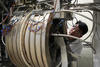 A researcher peers around the edge of large cylindrical piece of equipment in the lab. 