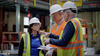 Three team members in construction safety gear stand talking inside the large warehouse where materials testing is taking place.