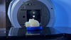 A model of a human head lies face up on the platform of an MRI machine. 