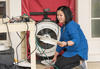 Lisa Ng kneels, holding parts of a circular fan built into a room divider. 