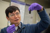 Researcher Ming Zheng looks with interest at a small vial he is holding up in front of him. 