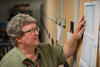 Doug White stands looking at a printed-out list taped to the end of a library shelf. 
