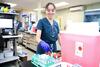 A medical worker in scrubs places a vial into a rack in a medical lab. 