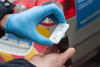 Close-up of a person wearing a blue medical glove holding a small handheld drug testing device in front of an emergency vehicle.