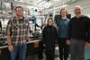 Four researchers pose smiling around a laser device on a lab table. 