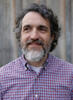 Nathan (Nate) D. Olson, a man with dark curly hair and a beard, smiling and glancing away from the camera in a professional outdoor headshot.