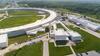 An arial view shows part of the huge enclosed loop of an accelerator, with attached buildings and parking lots.