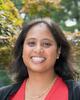 Sumona Sarkar, a woman with long brown hair, smiling for a professional headshot in front of a sun dappled tree.