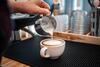 A barista pours steamed milk into a cup of espresso.