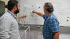 Two men face away from the camera, pointing to diagrams written on a whiteboard. 